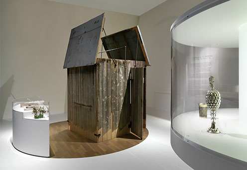 Blick in die Ausstellung: in der Bildmitte ist eine Sukka (Laubhütte) zu sehen, rechts und links sind Vitrinen mit weiteren Objekten