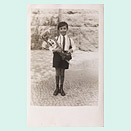 Ein sechsjähriger Junge in kurzen Hosen und mit einer Schultüte im Arm lächelt etwas verlegen in die Kamera