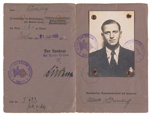 Aufgeklappte Doppelseiten eines grauen Ausweises mit handschriftlichen Eintragungen, Stempeln und Passfoto eines jungen Mannes im Anzug