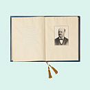 Aufgeschlagenes Buch, auf der rechten Seite eine Porträtfotografie eines schnurbärtigen Mannes in dunklem Anzug mit Fliege
