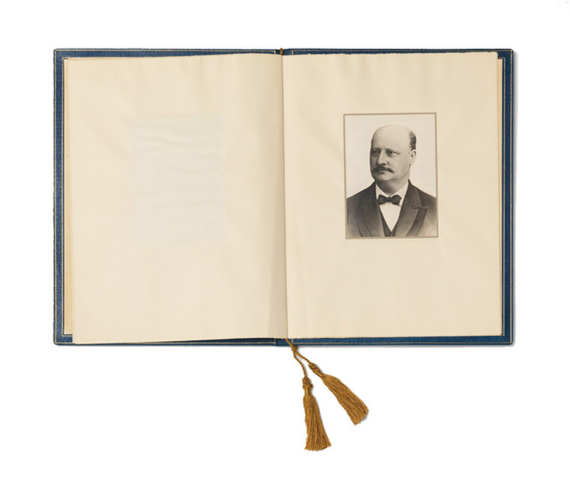 Aufgeschlagenes Buch, auf der rechten Seite eine Porträtfotografie eines Mannes in hellem Anzug mit Krawatte