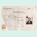 Ausweisformular in Frakturschrift, handschriftlich ausgefüllt. Im dafür vorgesehenen Feld ist das Passfoto eines Kindes aufgeklebt, das in den Ecken gelocht und mit Stempeln versehen ist.