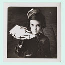 Photograph of a little girl in a shiny suit and cap balancing a tray of business cards on one hand.