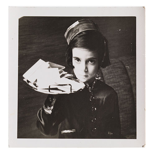 Photograph of a little girl in a shiny suit and cap balancing a tray of business cards on one hand.