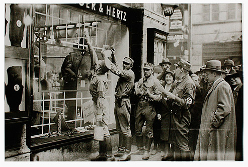 Members of the SA standing in front of a shop window with a bucket, brush and leaflets. Passers-by are looking on with expressions ranging from interested to gleeful.