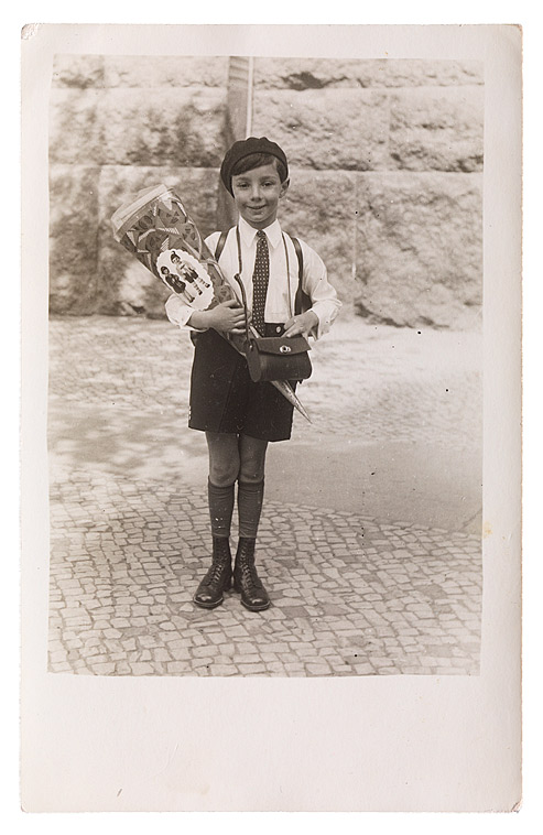 A six-year-old boy in shorts holding a cone full of candy and smiling sheepishly at the camera.