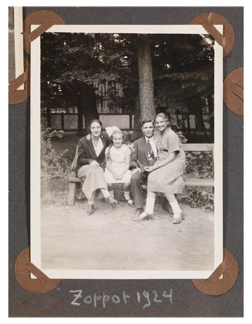 A family sitting on a park bench. The parents and two daughters are dressed in summer clothes and look cheerfully towards the camera.
