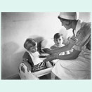 A nurse feeding two toddlers in children‘s chairs.