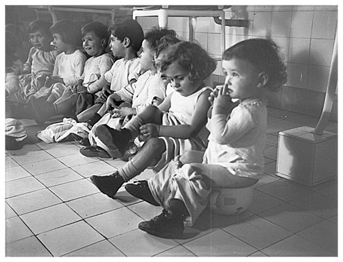 Eight small children sitting in a row on potties.