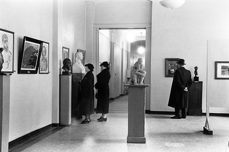 Exhibition room with displayed objects (paintings and sculptures) and visitors