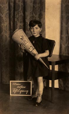 Girl with short hair and a school bag in front of a table, to the left a small chalkboard reading My first day of school