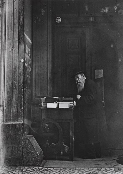 Black-and-white photo of an elderly man with a table of books in the buildings entrance