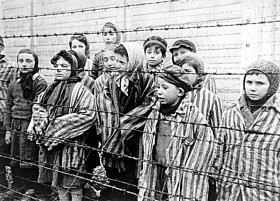 Black-white photograph of surviving children of the concentration camp in Auschwitz standing behind a fence