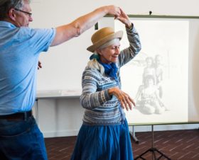 Photo of the dance scene described in the text, in the background a canvas with beach photo