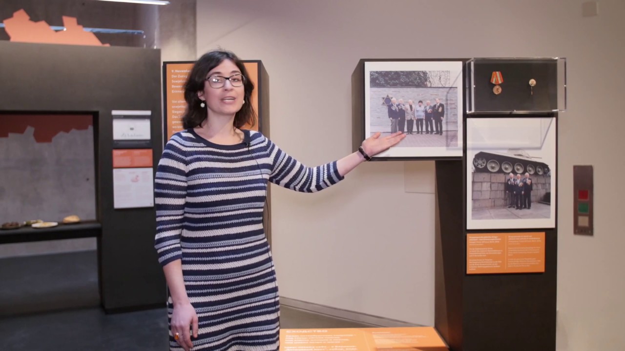 Frau mit geringeltem Kleid zeigt auf ein Bild in einer Ausstellung.