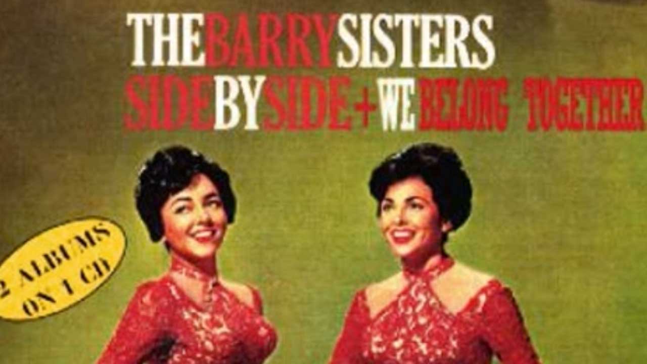 Album cover of the Barry Sisters. Two women in red dresses stand laughing against a railing. 