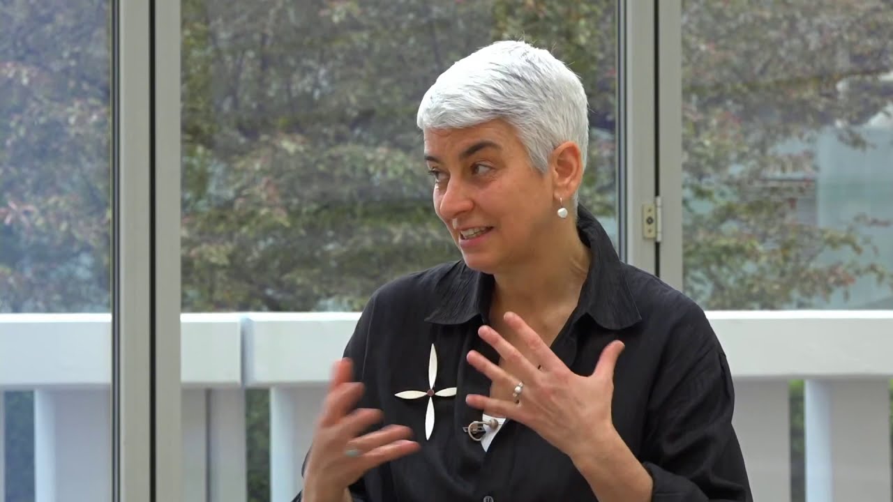 Woman with white hair gestures with both hands.