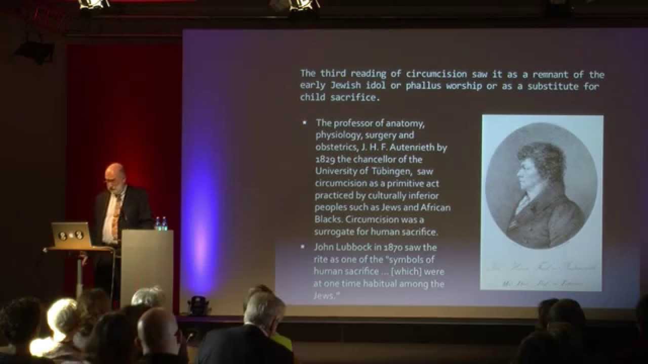 Man at the lectern, behind him a slide of his presentation.