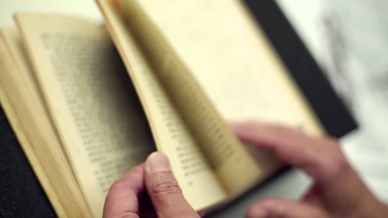 A pair of hands flip through an old book with yellowed pages.