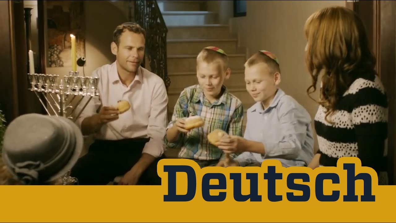 A family sits in the living room in front of an eight-branched candlestick and is pastry.