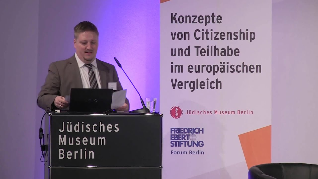 Man in suit and tie stands at lectern and gives a lecture.