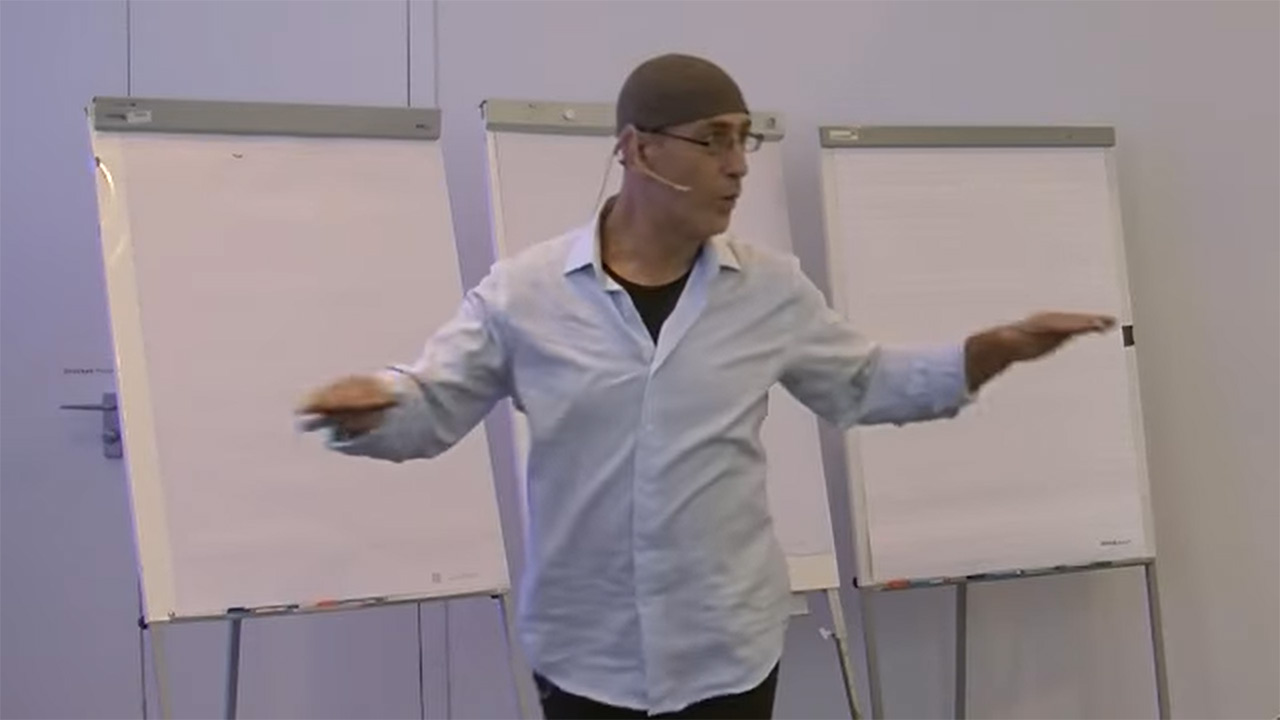 Man in front of three flipcharts moderates a workshop.