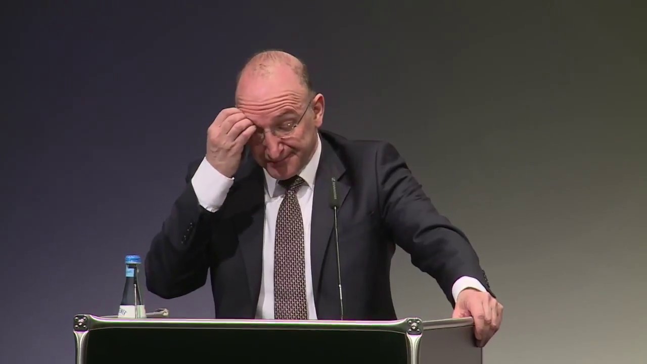 A man stands at the lectern and looks at his manuscript.