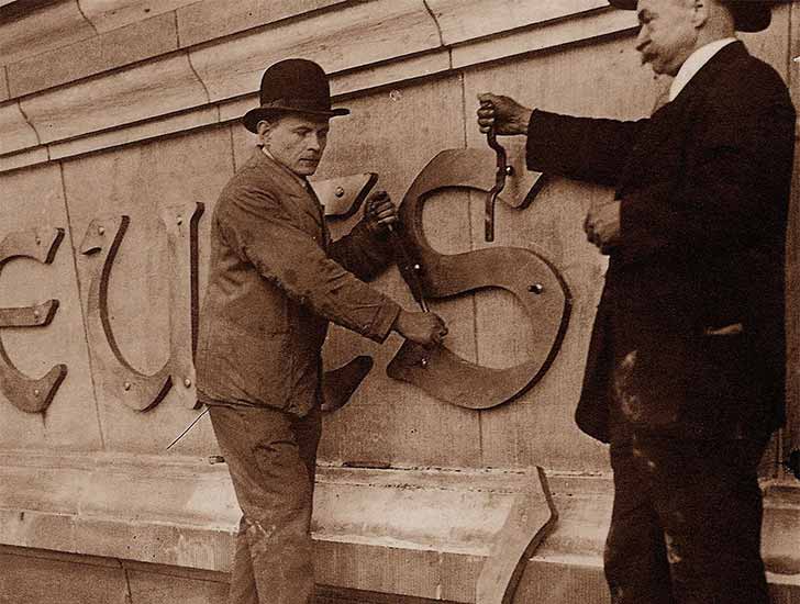 Craftsmen with tools apply lettering to a facade