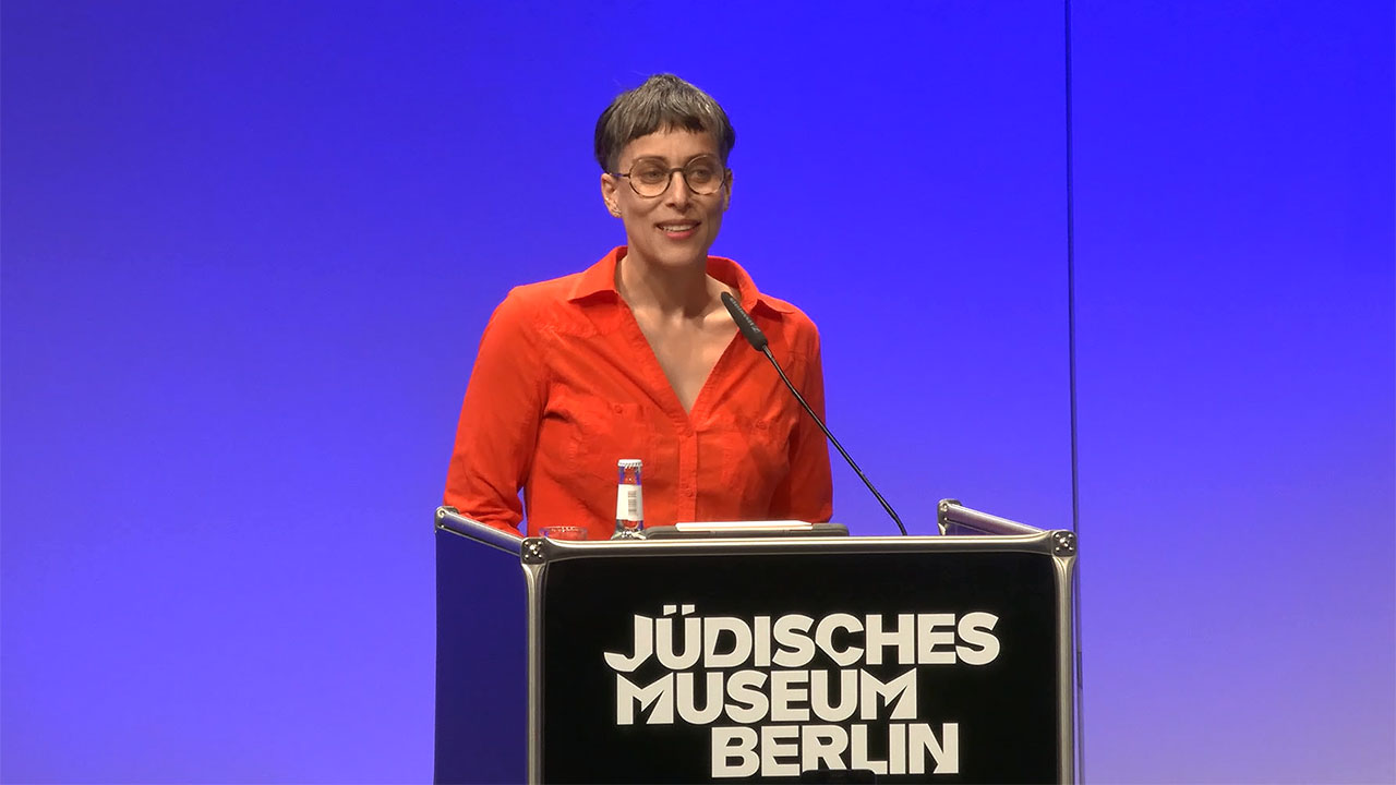 Woman in red shirt stands at a lectern.