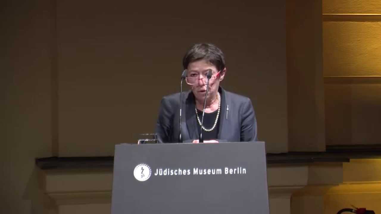 A woman with glasses stands at the lectern and speaks.