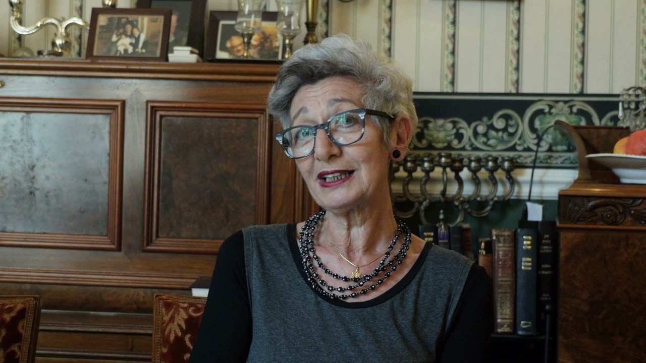 A woman in an armchair speaks into the camera.