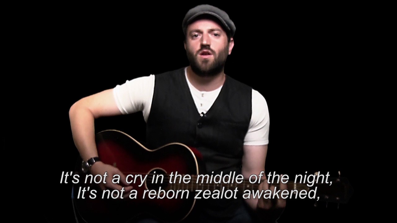 Man with cap plays on a guitar and sings.