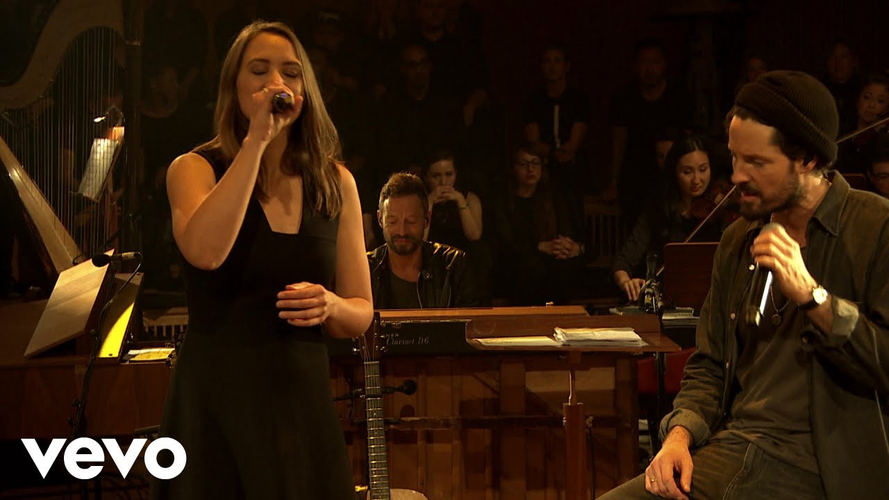 A woman and a man stand on a stage and sing.