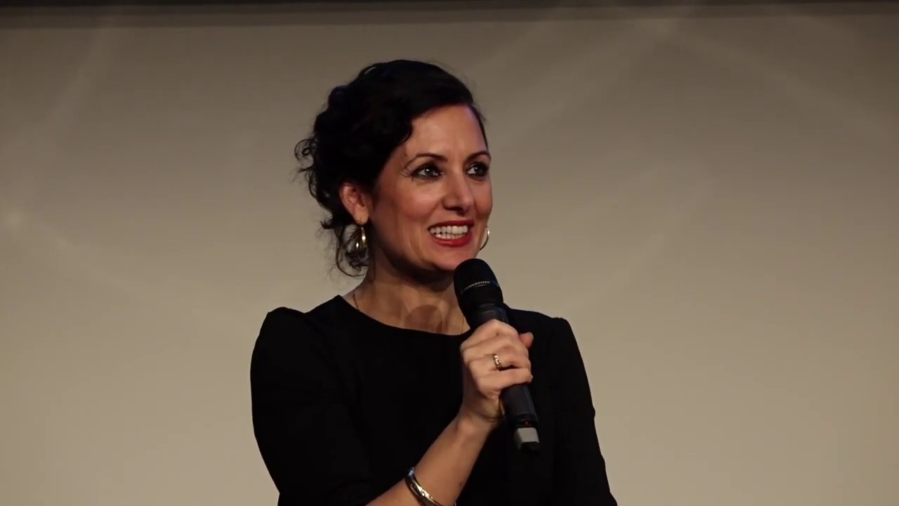 Woman with dark hair and black dress is holding a microphone.
