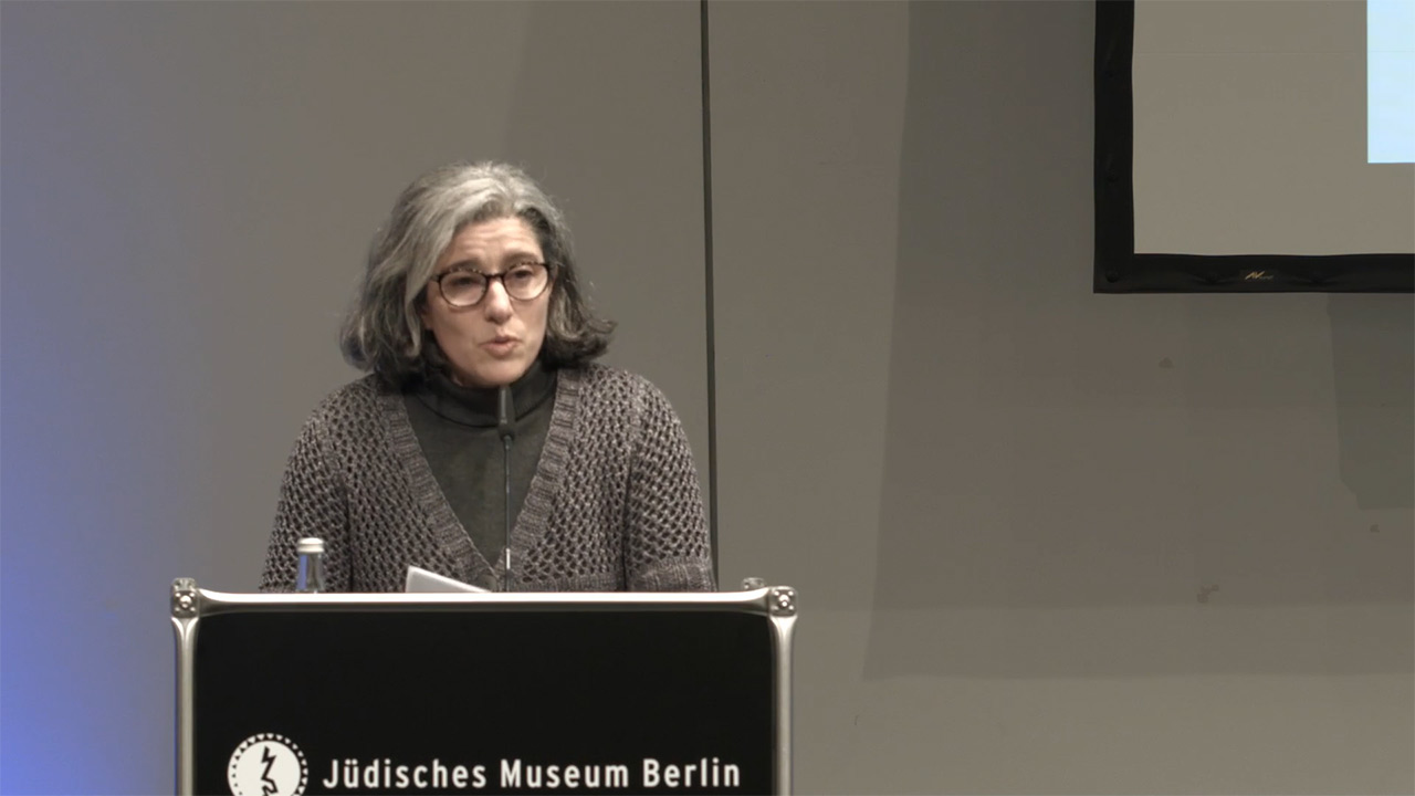 Woman at lectern speaks in front of audience.