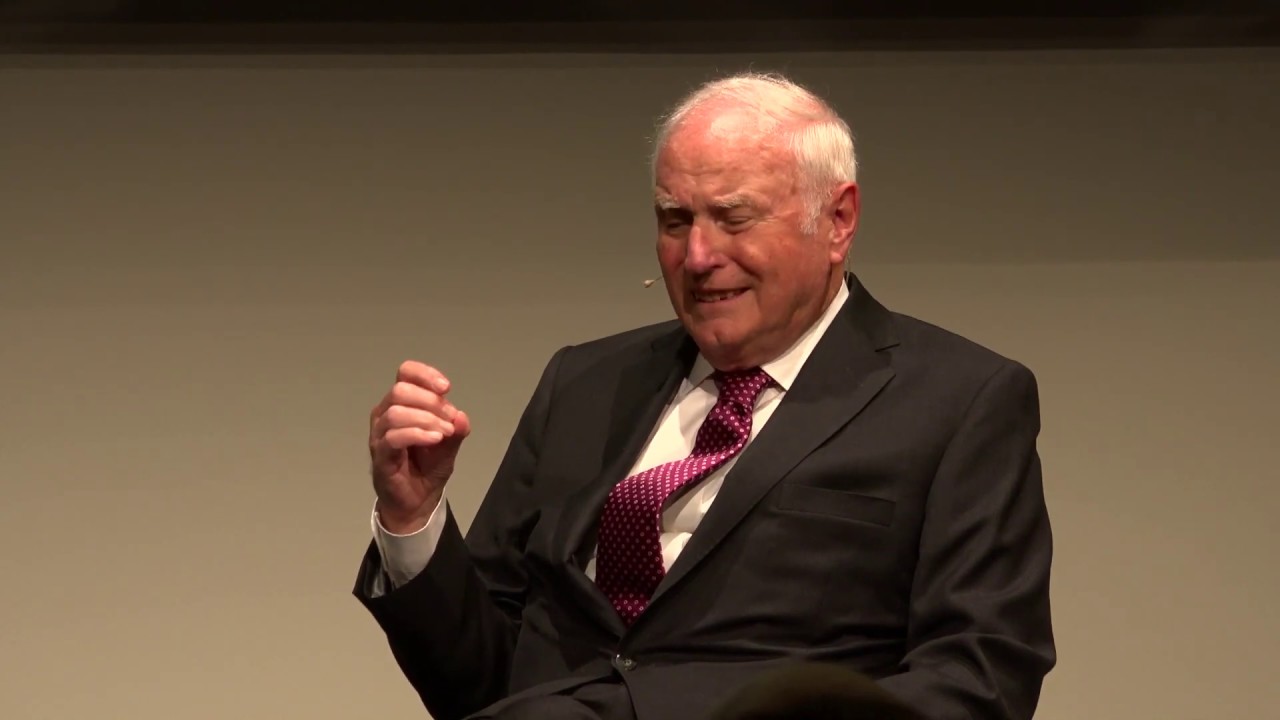 Man in suit and tie gesticulating with one hand.