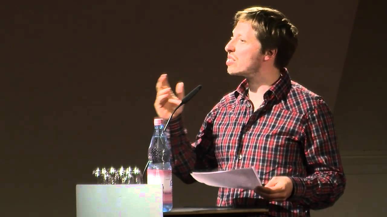 Ein Mann auf einer Bühne hinter einem Pult hält eine Rede.