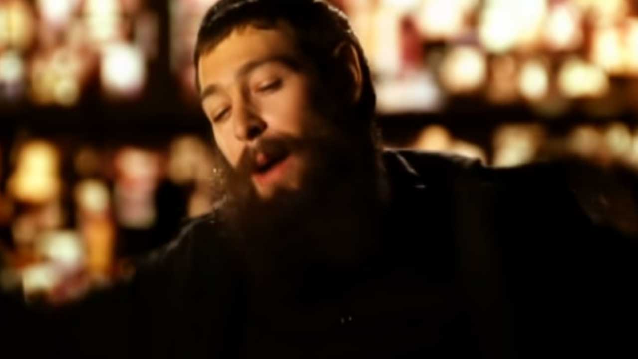 Shot of a singer with a long beard in dark clothing. Blurred lights are visible in the background.
