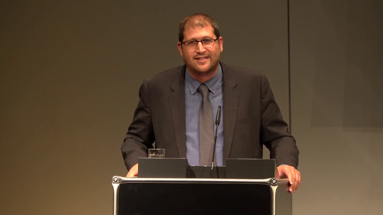 A man stands at the lectern and looks into the audience.