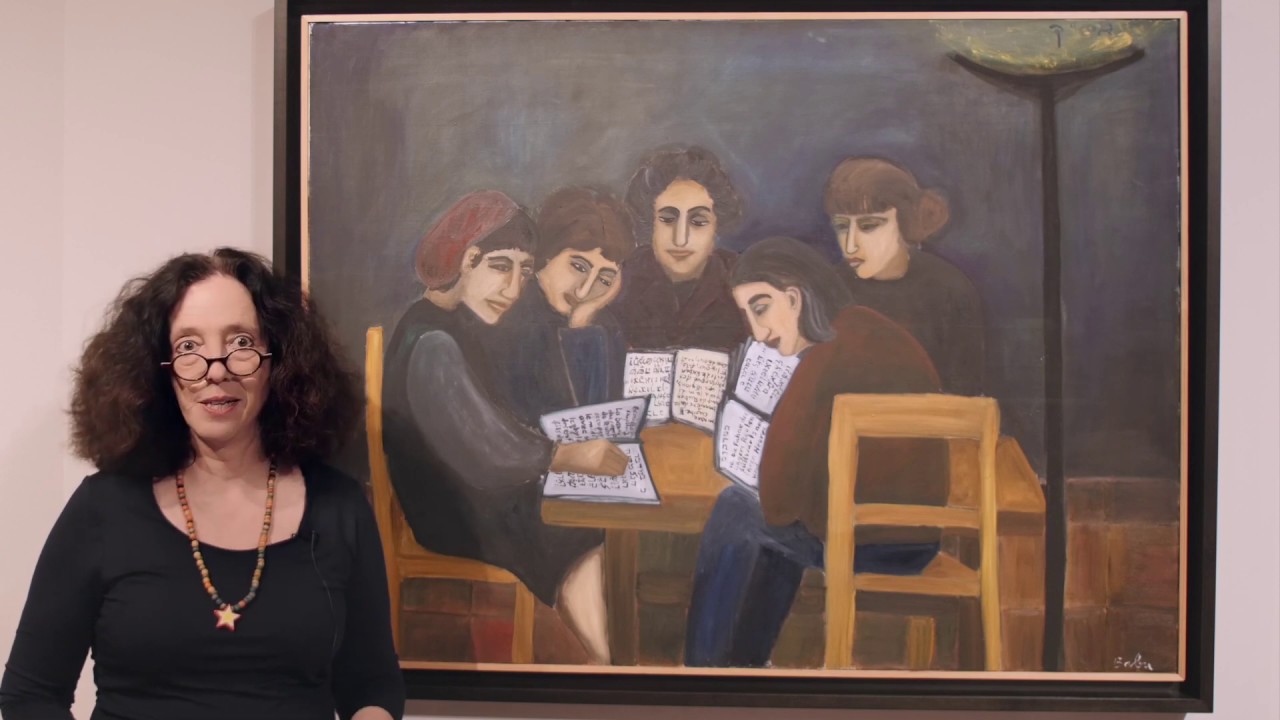 Woman with glasses and star necklace stands in front of a painting and looks friendly into the camera.