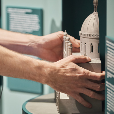 A pair of hands feeling a model of a synagogue