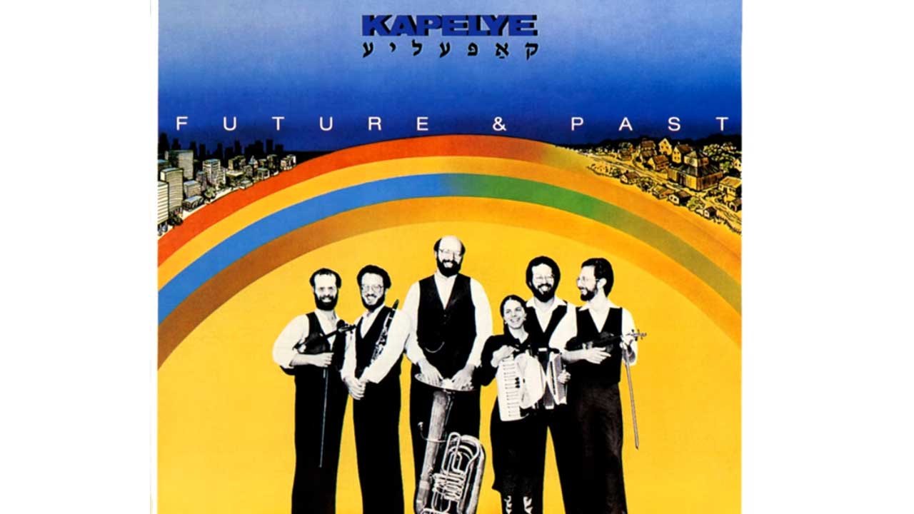 Album cover of the band Kapelye. The six-member band is inserted in black and white tones against a yellow graphic. The members are holding their instruments. Further up the graphic is a rainbow, with houses drawn to the left and right.