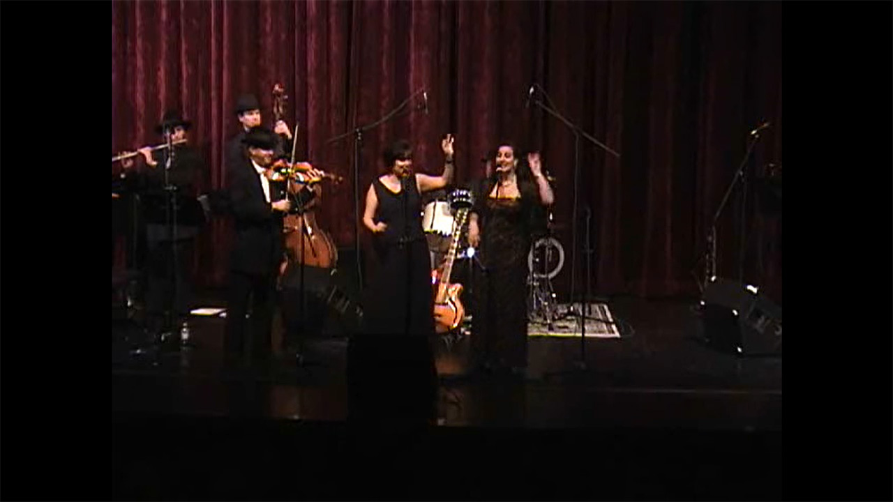 Eine Musikband mit fünf Musiker*innen stehen auf einer Bühnen.