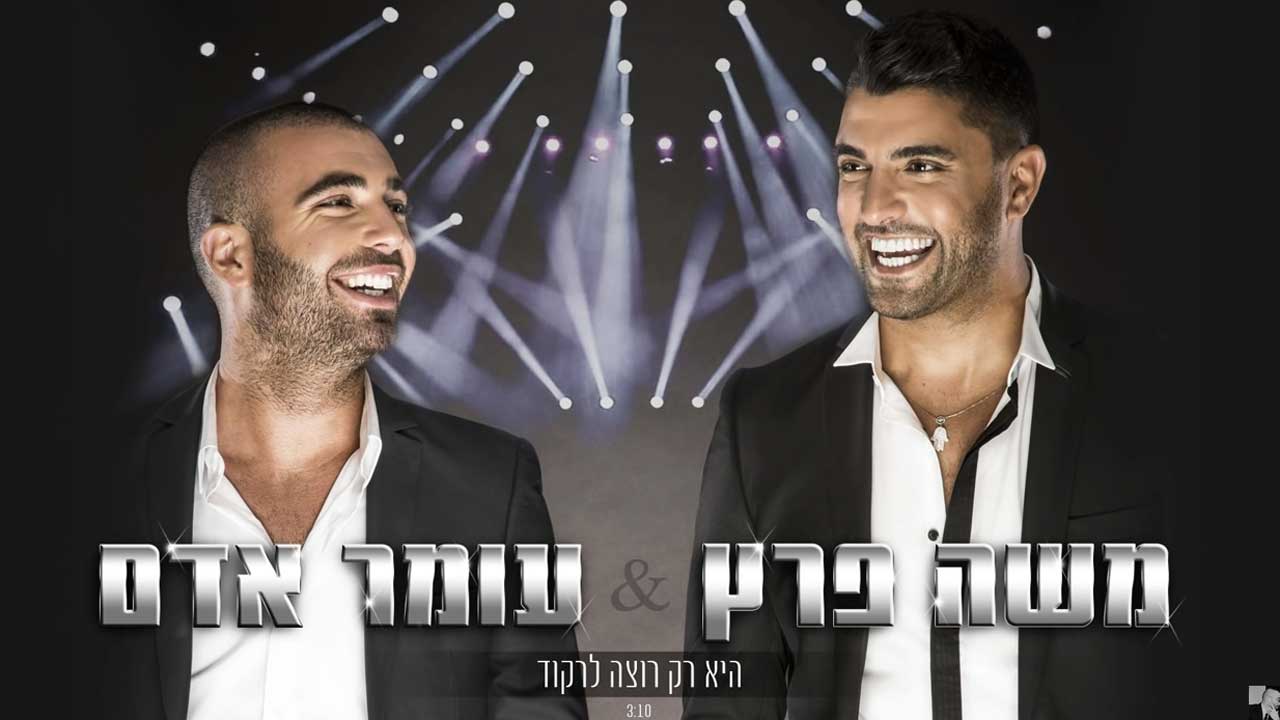 Two singers in white shirts and jackets are laughing. Spotlights can be seen in the background.
