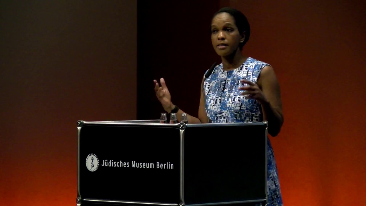 A woman stands at the lectern and speaks gesticulating with both hands.