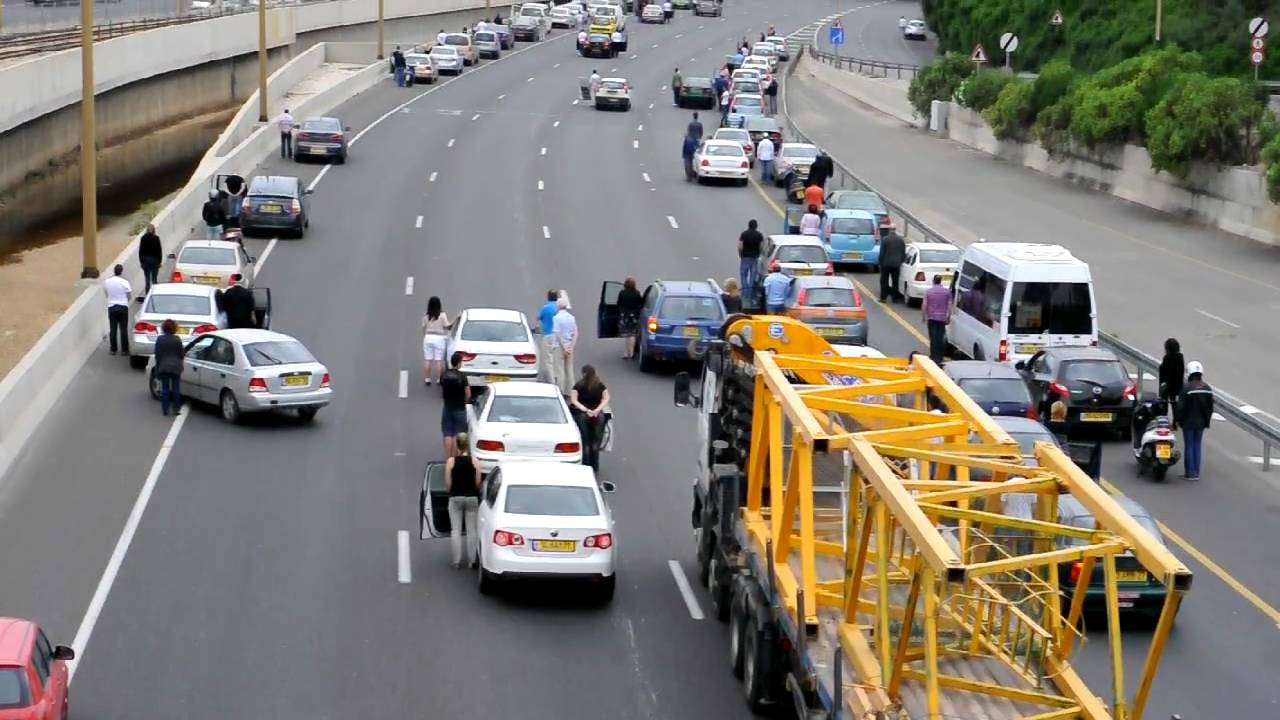 A four-lane road where all cars have stopped and people are standing next to their vehicles.