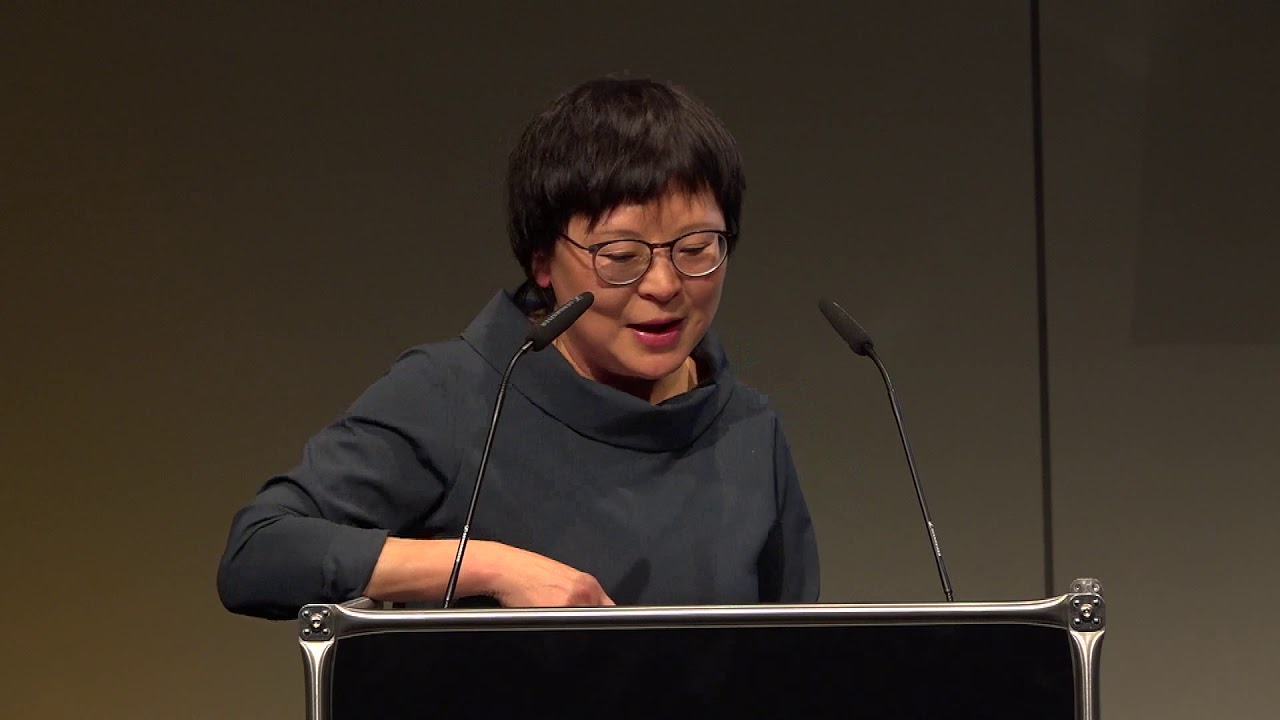 Woman at lectern speaks in front of audience.