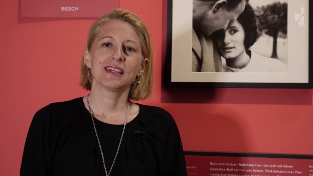 Woman stands in front of a black and white photo in an exhibition and looks friendly into the camera.