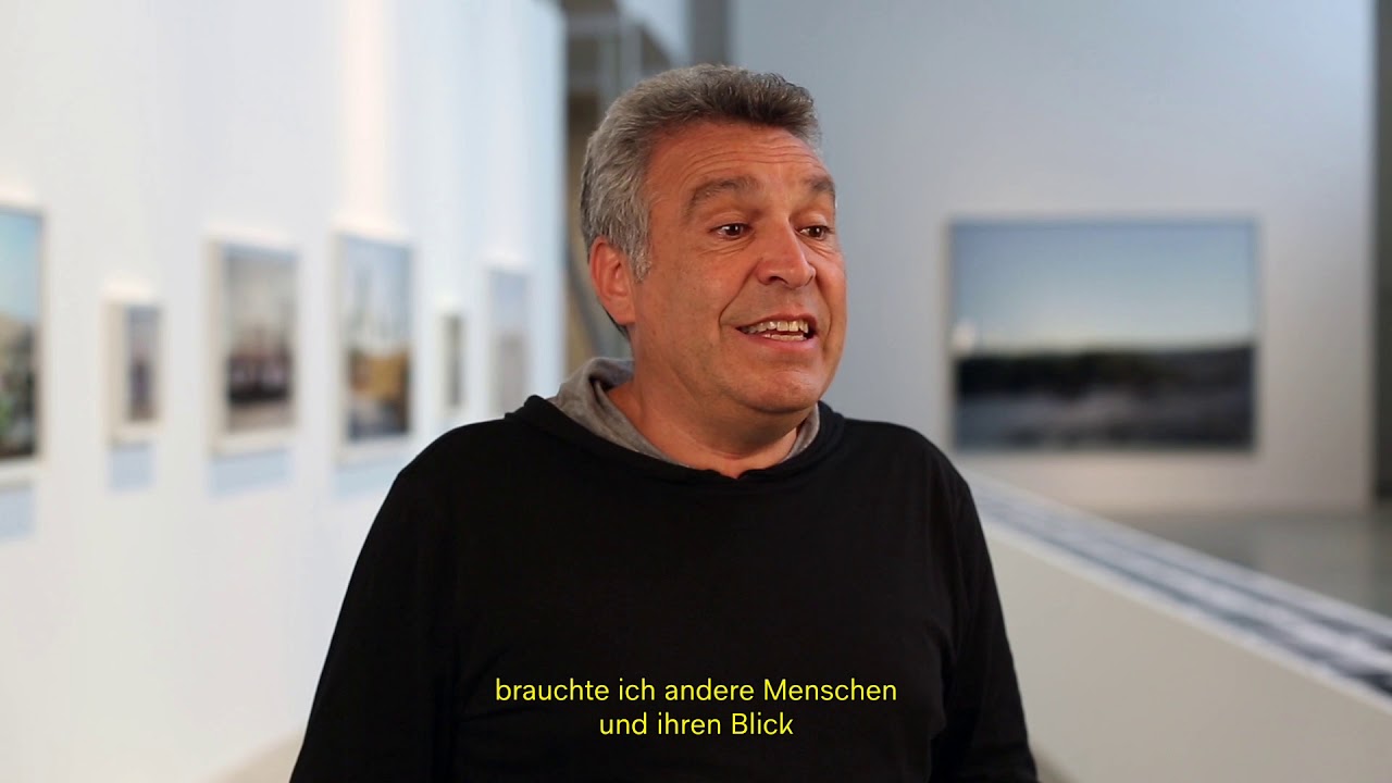 Mann mit schwarzem Pullover in Interviewsituation vor der Kamera.