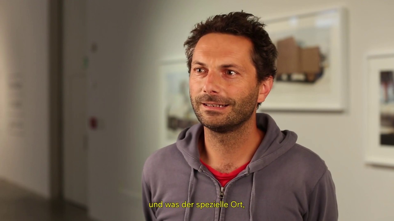 Man with gray sweatshirt stands in an exhibition.